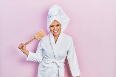 Bornoz giyen genç İspanyol kız sünger tutuyor. Pozitif ve mutlu görünüyor. Kendine güvenen bir gülümsemeyle dişlerini gösteriyor. 