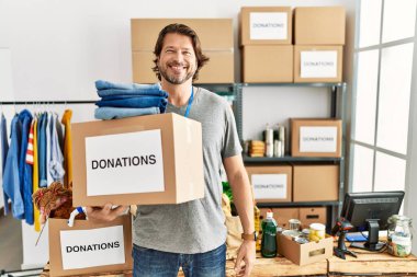 Gönüllü standında bağış kutusunu tutan yakışıklı, orta yaşlı bir adam. Yüzünde mutlu ve havalı bir gülümsemeyle. şanslı kişi. 