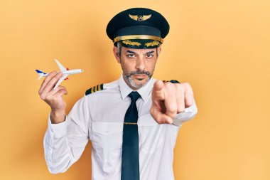 Yakışıklı, orta yaşlı, gri saçlı, uçak pilotu üniforması giyen, elinde oyuncak uçak tutan, kamerayı işaret eden, kendine güvenen, ciddi görünümlü bir adam. 