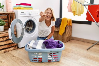 Çamaşırlarını sepete koyup çamaşır yıkayan beyaz bir kadın. Kameraya kızgın ve sinirli. 