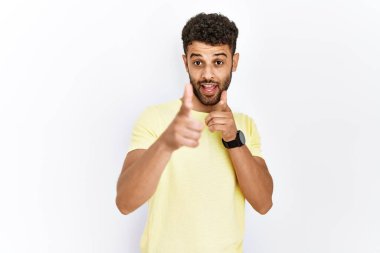 Arap genç adam izole edilmiş arka planda durup mutlu ve komik yüzlü parmakları kameraya doğrultuyor. iyi enerji ve titreşimler. 