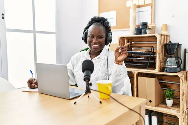 在电台演播室工作的年轻的非洲女人高兴地微笑着 手指手画脚地指向一边 — 图库照片