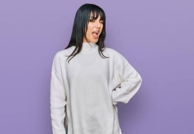 Kâküllü, balıkçı yaka kazak giyen genç esmer kadın kameraya seksi bir ifadeyle bakıyor, neşeli ve mutlu bir yüzle.. 