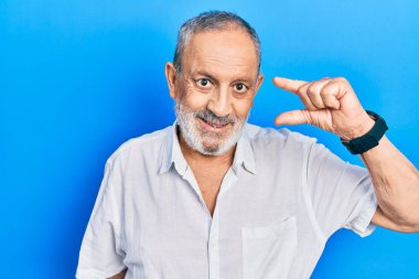 Sakallı, sıradan, beyaz tişörtlü, kendine güvenen, el hareketi yapan, küçük beden işareti yapan, parmaklarını gösterip kameraya bakan yakışıklı bir adam. ölçüm kavramı. 