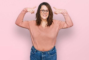 Gündelik kıyafetler giyen ve gözlüklü genç bir kadın iki eliyle başını gösteren gülümseme, harika bir fikir veya düşünce, iyi bir hafıza 