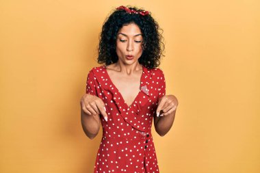 Yazlık elbise giyen genç Latin kız parmaklarını göstererek reklamını yapıyor, şaşırmış yüz ve ağzını açıyor. 