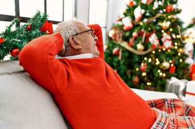 Yaşlı, kır saçlı, elleri başının üstünde rahatlamış evde Noel 'i kutluyor..