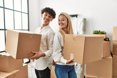 Genç ve güzel bir çift mutlu bir şekilde gülümsüyor. Yeni evlerinde karton kutu tutuyorlar..