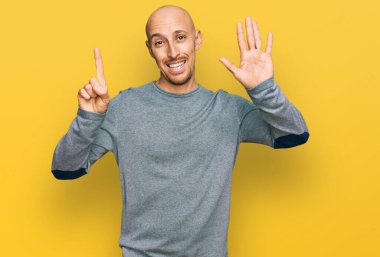 Kel, sakallı, günlük giysiler giyen, altı numaralı parmaklarıyla işaret eden, kendinden emin ve mutlu bir şekilde gülümseyen adam.. 
