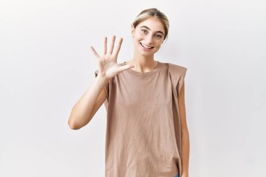 İzole edilmiş arka planda duran genç sarışın kadın beş numarayı gösterip işaret ederken kendinden emin ve mutlu gülümsüyor.. 