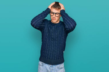 Sıradan kıyafetler ve gözlük takan genç sarışın adam baş ağrısı ve stres yüzünden acı çekiyor çünkü acı ve migren. Eller başının üstünde.. 