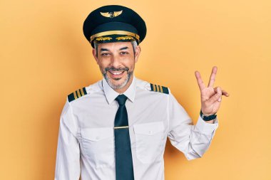 Yakışıklı, orta yaşlı, gri saçlı, uçak pilotu üniforması giyen, kameraya bakıp zafer işareti yapan bir adam. İki numara.. 