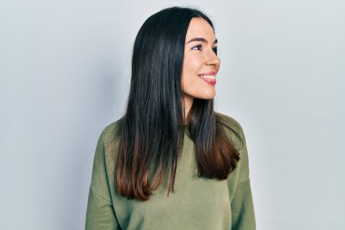 Genç esmer kadın, günlük yeşil süveter giyiyor. Yüzünde gülümseme, doğal bir ifade ile yan yana bakıyor. Kendinden emin gülen. 