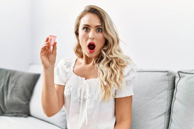 Sarışın genç bir kadın elinde regl fincanı tutuyor. Korkmuş ve şaşırmış bir şekilde ağzı açık, inançsız bir yüz. 