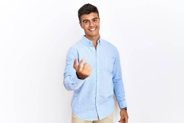 İspanyol iş gömleği giyen genç adam izole edilmiş arka planda dikiliyor. Buraya el hareketleriyle mutlu bir şekilde karşılamaya ve gülümsemeye davet ediyor. 