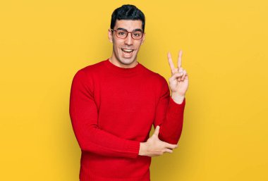 Yakışıklı İspanyol bir adam günlük kıyafetler ve gözlük takıyor. Gülümsüyor ve kameraya göz kırpıyor. Zafer işareti yapıyor. İki numara.. 