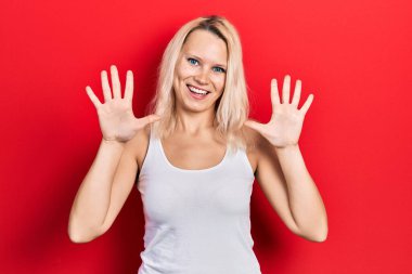 Güzel, beyaz tişört giyen beyaz tenli sarışın kadın on numarayı gösterip işaret ederken kendinden emin ve mutlu bir şekilde gülümsüyor.. 