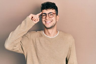 Gündelik kıyafetler ve gözlük takan genç İspanyol bir adam tek parmakla kafasını işaret ediyor, harika bir fikir ya da düşünce, iyi bir hafıza. 