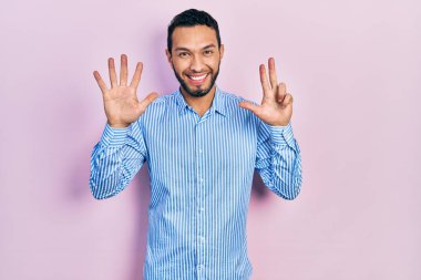 Sakallı, sıradan mavi tişörtlü İspanyol bir adam 8 numaralı parmaklarını gösterip gösterirken kendinden emin ve mutlu bir şekilde gülümsüyor.. 