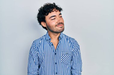 Gündelik kıyafetler giyen genç İspanyol bir adam yüzünde gülümsemeyle yan yana bakıyor, doğal bir ifade. Kendinden emin gülen. 