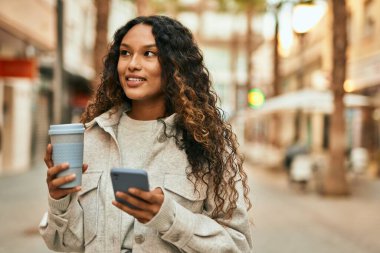 Genç Latin kadın akıllı telefon kullanıyor ve şehirde kahve içiyor..