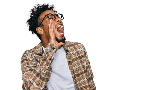 ひげを生やした若いアフリカ系アメリカ人の男性は カジュアルな服や眼鏡を着て大声で叫び 口の上で手で横に叫んでいます コミュニケーションの概念 — ストック写真