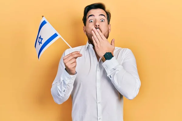 英俊的高加索人 留着胡子 手拿着覆盖着嘴的以色列国旗 感到震惊和害怕犯错 惊讶的表情 — 图库照片