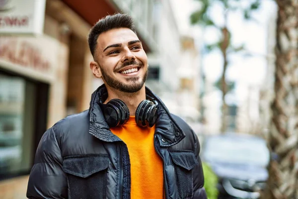 Sakallı yakışıklı, neşeli ve kendine güvenen, kışlık palto ve kulaklık takan bir İspanyol.