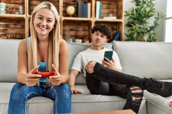 Young couple smiling happy playing video game and using smartphone at home.