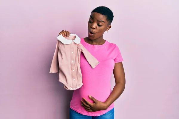 Mujer Afroamericana Joven Esperando Bebé Sosteniendo Ropa Asustado Sorprendido Con — Foto de Stock