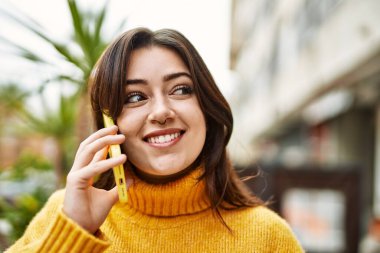 Açık havada balıkçı yaka kazak giyen güzel esmer kadın telefonda konuşuyor.
