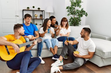 Partide gülümseyen ve evde klasik gitar çalan bir grup genç arkadaş..