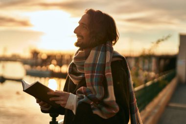 Genç İspanyol adam gülümseyerek limanda mutlu bir kitap okuyor..
