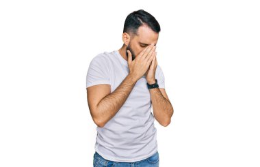 Sakallı, günlük beyaz tişörtlü, suratını ellerle kapatıp ağlayan genç bir adam. depresyon kavramı. 
