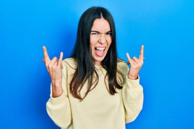 Genç esmer kadın, sıradan bir kazak giyip çılgın bir ifadeyle bağırıyor ve elleri havada rock sembolü yapıyor. Müzik yıldızı. ağır kavram. 