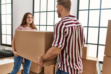 Genç beyaz çift mutlu bir şekilde gülümsüyor. Yeni evlerinde karton kutu tutuyorlar..