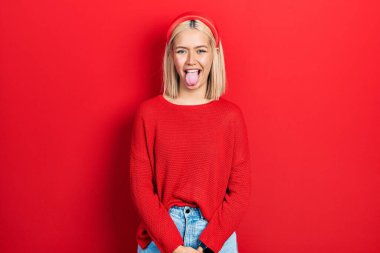 Kırmızı süveter giyen güzel sarışın kadın komik bir ifadeyle dilini dışarı çıkartıyor. duygu kavramı. 