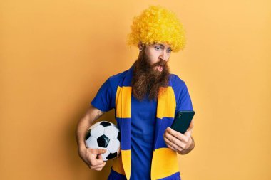 Kızıl saçlı, uzun sakallı futbol holiganları tezahürat yapıyor. Şok olmuş suratına akıllı telefon doğrultuyor. Şüpheci ve alaycı bakıyor. 