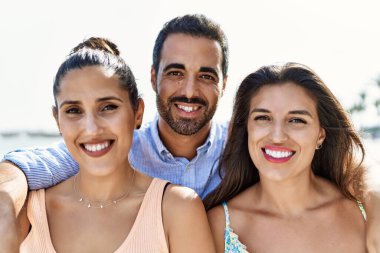 Mutlu gülümseyen ve kumsalda sarılan üç İspanyol genç arkadaş..