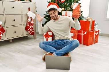 Genç İspanyol adam mutlu bir şekilde gülümsüyor. Yılbaşı hediyesi olarak evde dizüstü bilgisayar kullanıyor..