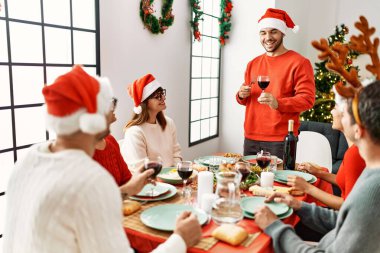 Mutlu bir şekilde gülümseyen bir grup genç Noel yemeği yiyor ve evde kadeh kaldırıyor..