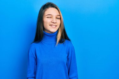 Balıkçı yaka kazak giyen genç esmer kız kameraya seksi bir ifadeyle bakıyor, neşeli ve mutlu bir yüzle.. 