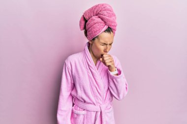 Duş başlığı ve bornoz takan genç sarışın kadın kendini kötü hissediyor ve soğuk algınlığı veya bronşitin belirtisi olarak öksürüyor. sağlık hizmeti kavramı. 