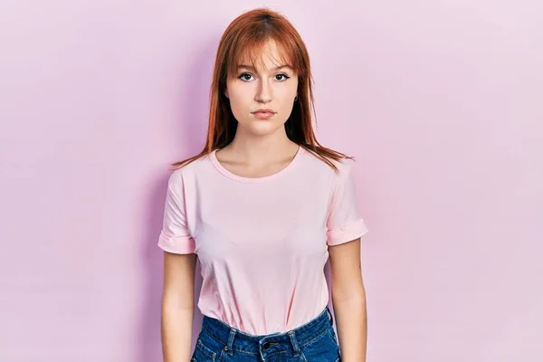 红头发的年轻女人穿着宽松的粉色T恤 脸上带着严肃的表情 简单而自然地看着相机 — 图库照片