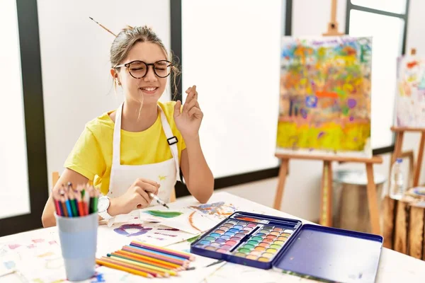 Young Brunette Teenager Art Studio Gesturing Finger Crossed Smiling Hope — Stock Photo, Image