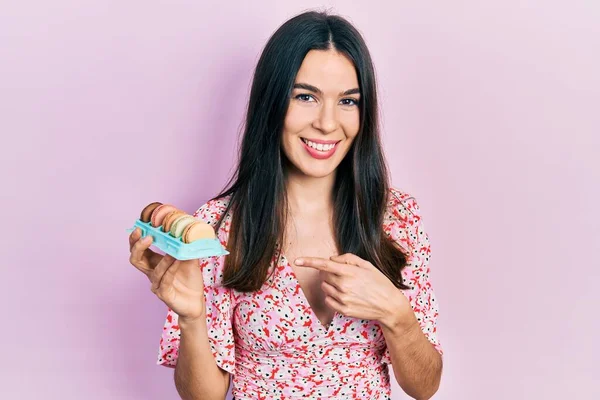 Joven Morena Sosteniendo Deliciosos Macarons Pasteles Sonriendo Feliz Señalando Con — Foto de Stock