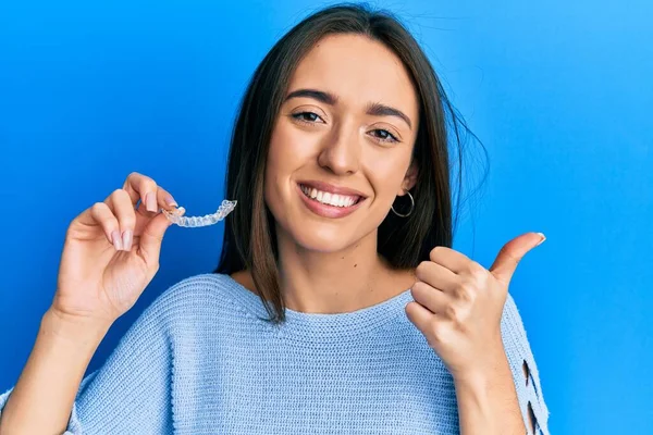 Joven Chica Hispana Sosteniendo Invisible Alineador Ortodoncia Apuntando Pulgar Hacia — Foto de Stock