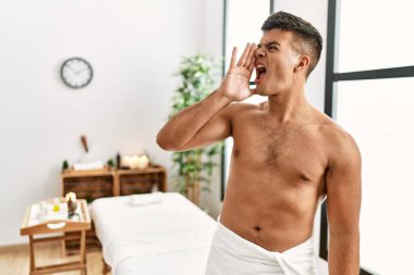 İspanyol asıllı genç adam spa merkezinde üstsüz duruyor ve el pençe divan durup bağırıyor. iletişim konsepti. 