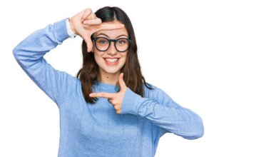 Gündelik kıyafetler ve gözlük takan, gülümseyen, elleri ve parmakları gülen yüzlü güzel bir kadın. yaratıcılık ve fotoğrafçılık kavramı. 