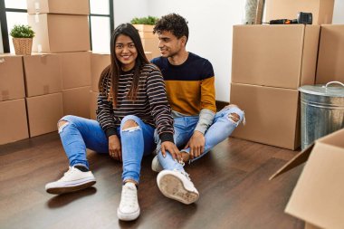 Young latin couple smiling happy sitting on the floor at new home.